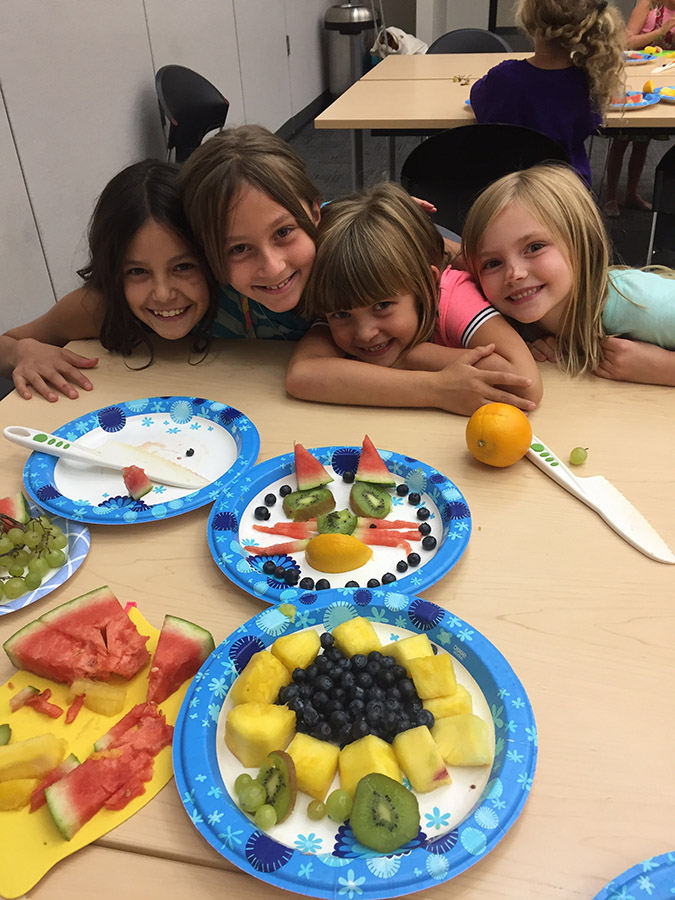 group of girls learning how to cut food in a sticky fingers cooking class